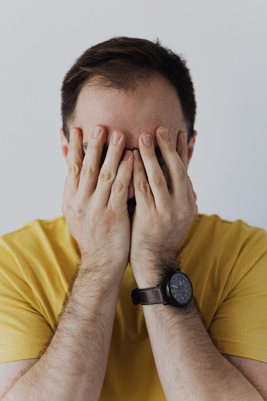 man in yellow shirt covering his face with his hands