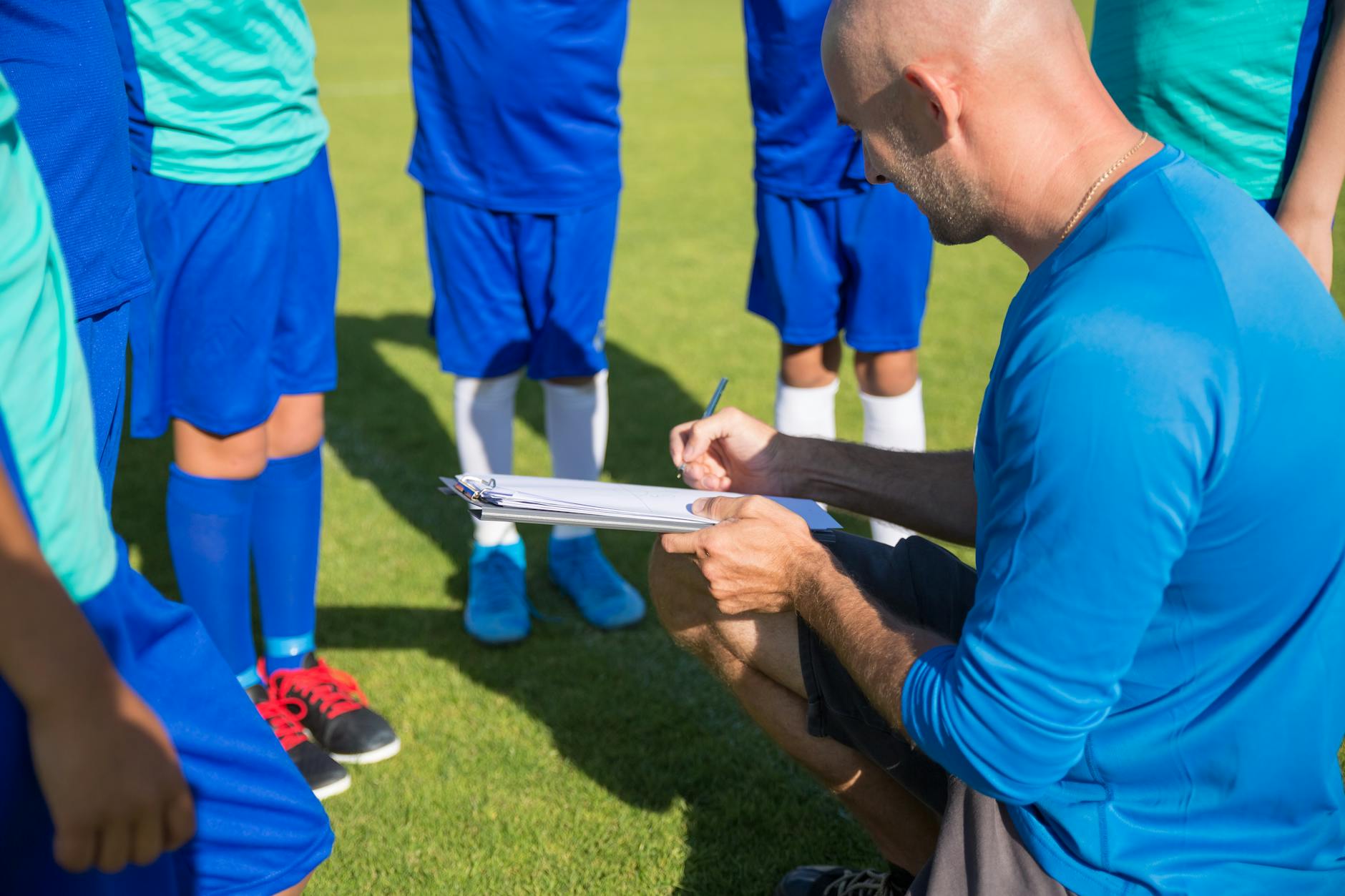 a man in blue shirt coaching a group of kids standing on a soccer field