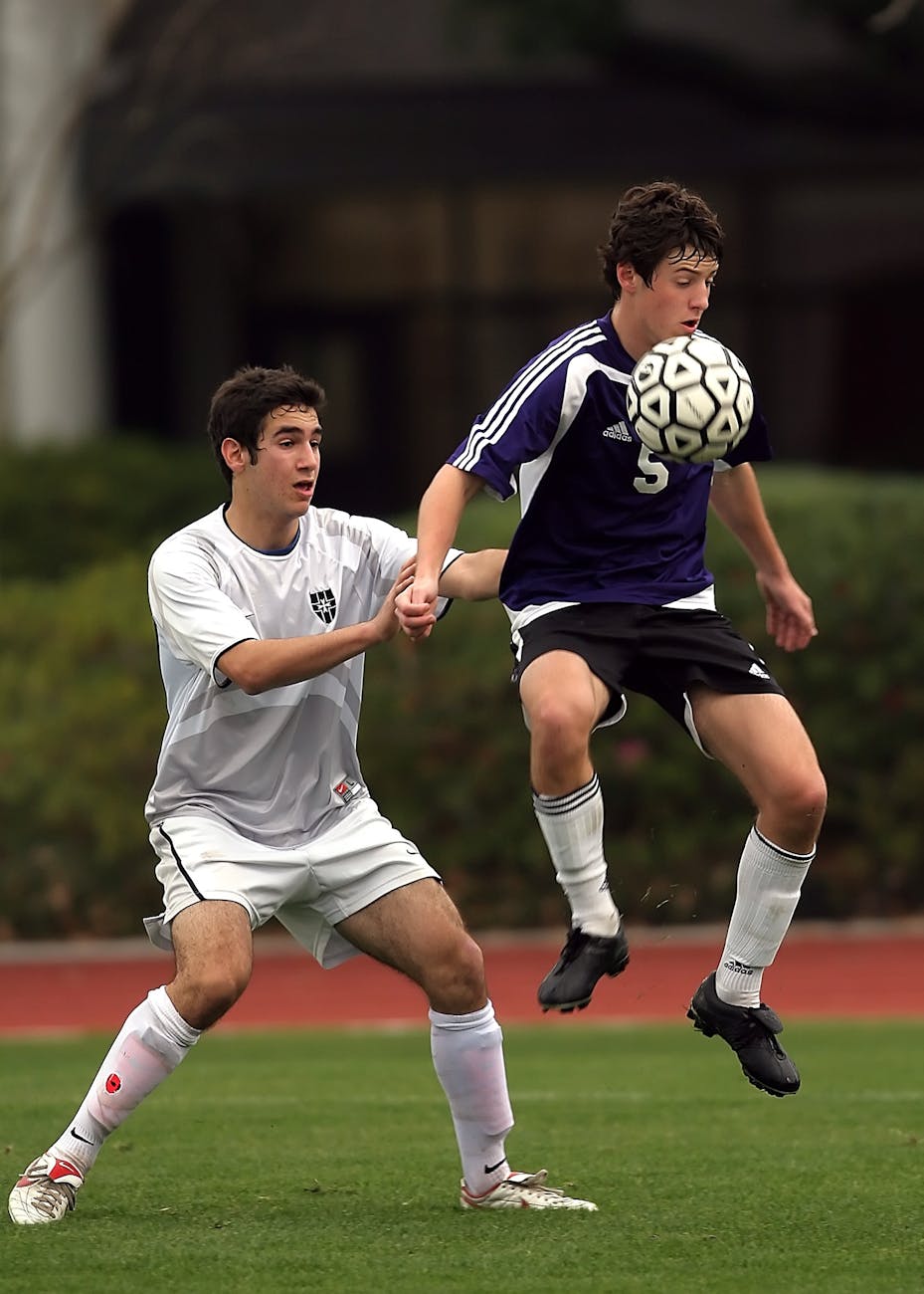 two men playing soccer at soccer field near green plants during daytime